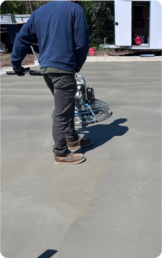 A worker is operating a concrete power float to finish and level a concrete slab